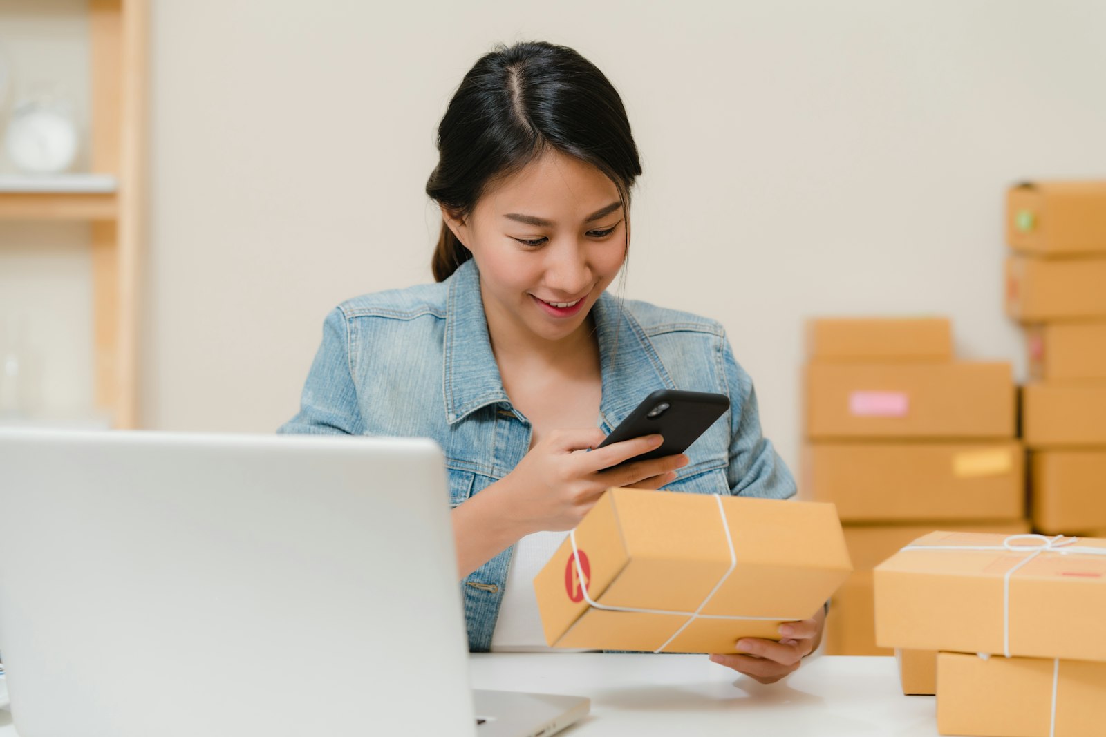 Online Shop eröffnen: Gründerin prüft ein Paket neben Laptop und Versandkartons