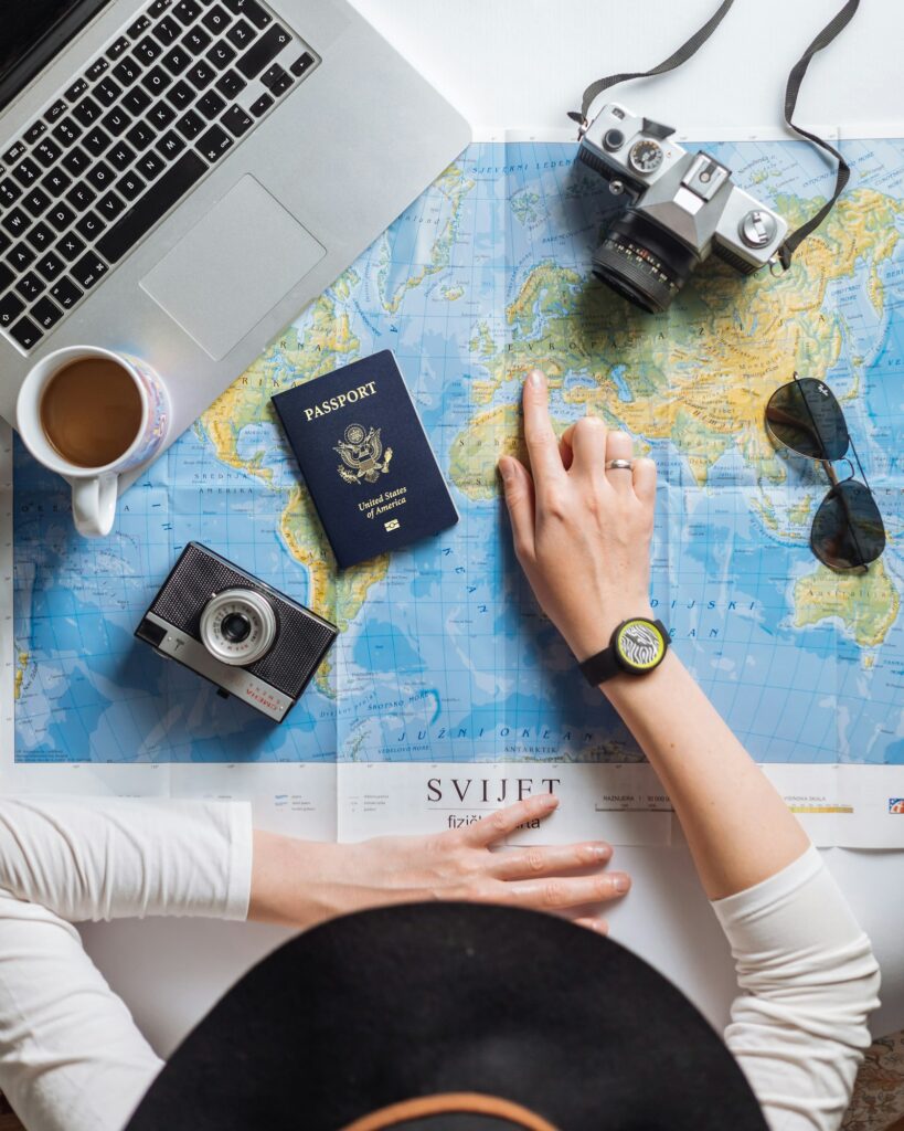 Person mit Reisepass, Kameras und Laptop über einer Weltkarte – Planung für einen Reiseblog