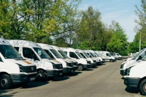 Reihe weißer Firmentransporter auf einem Parkplatz, deren Nutzung ein elektronisches Fahrtenbuch erfasst