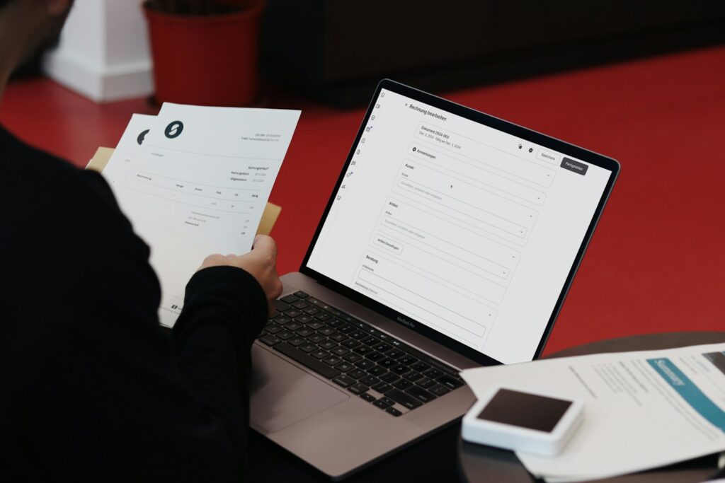 Person arbeitet am Schreibtisch mit Laptop und Papieren an der Buchhaltung im Startup