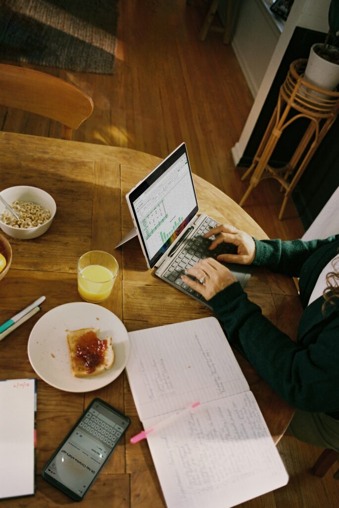 Person arbeitet mit Laptop am Holztisch beim Frühstück im Homeoffice