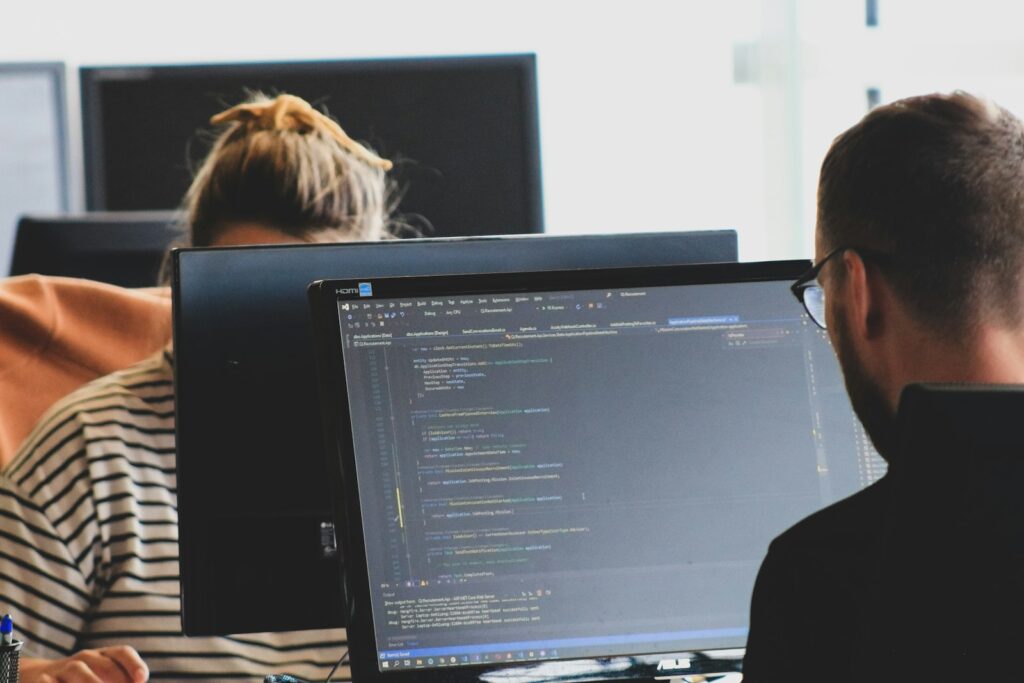 Zwei Entwickler arbeiten in einem hellen Büro gemeinsam an Programmcode auf mehreren Monitoren