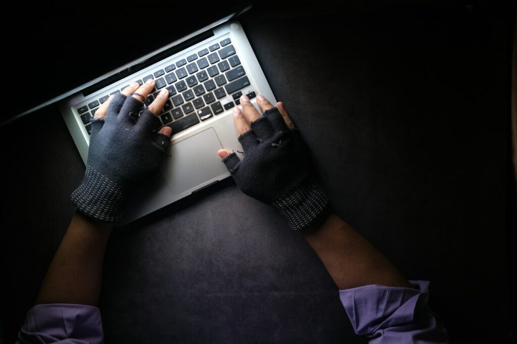 Person mit Handschuhen tippt nachts auf einem Laptop, typisches Bild für Cyberkriminalität
