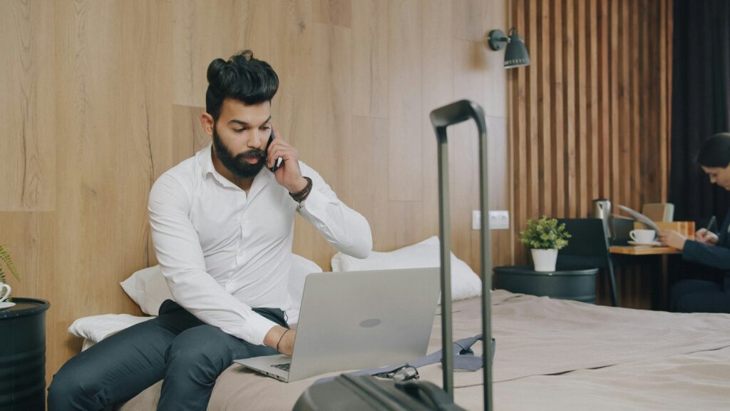 Geschäftsreisender telefoniert im Hotelzimmer und arbeitet dabei am Laptop