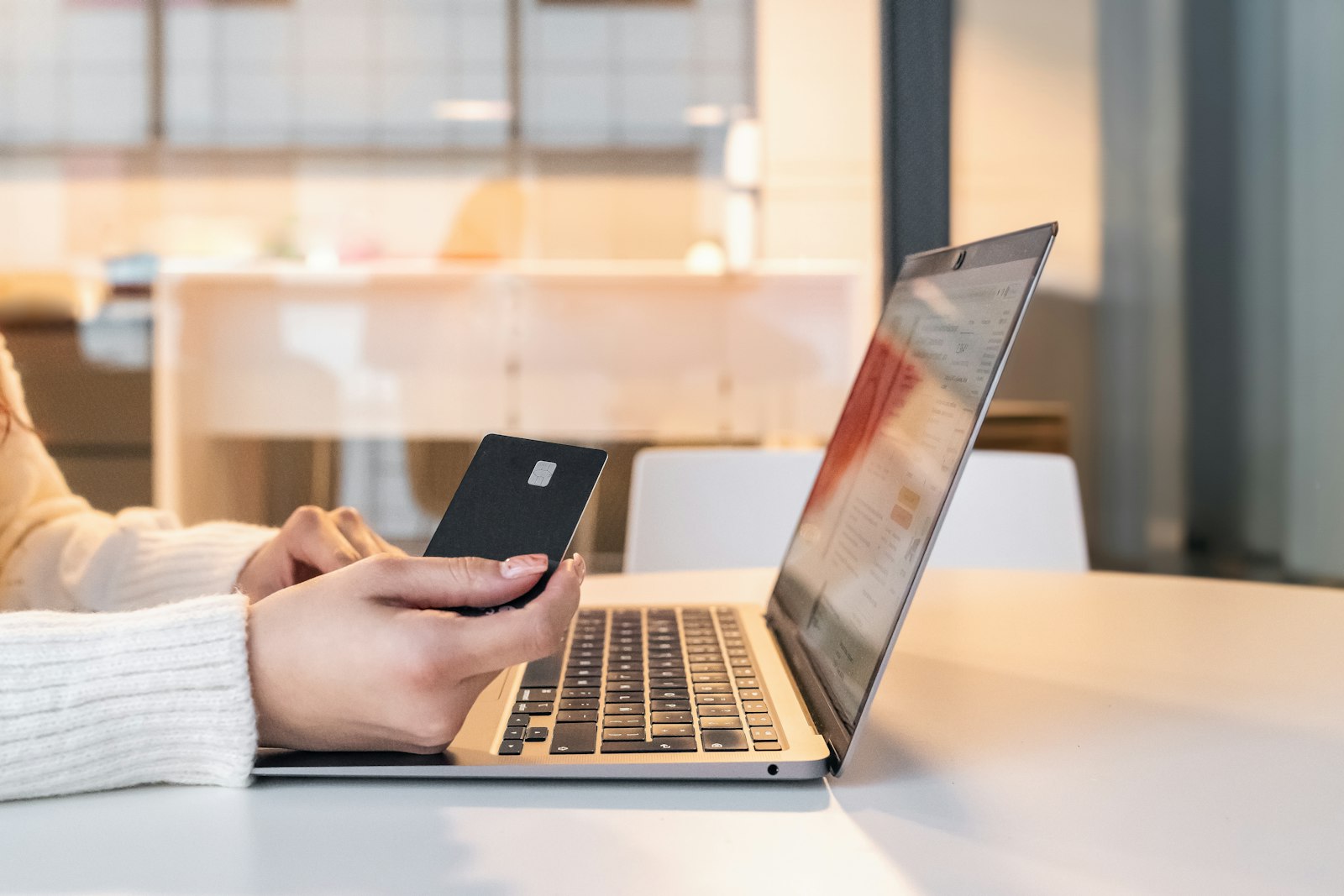 Frau sitzt am Laptop und bestätigt mit dem Smartphone eine Zahlung per Open Banking