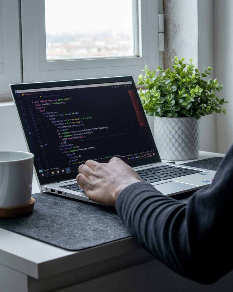 Person programmiert am Laptop neben einer Topfpflanze und baut den Tech-Stack eines Startups auf
