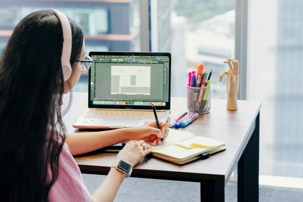 Frau mit Kopfhörern lernt am Schreibtisch – E-Learning-Entwicklung für flexible Mitarbeiterschulungen